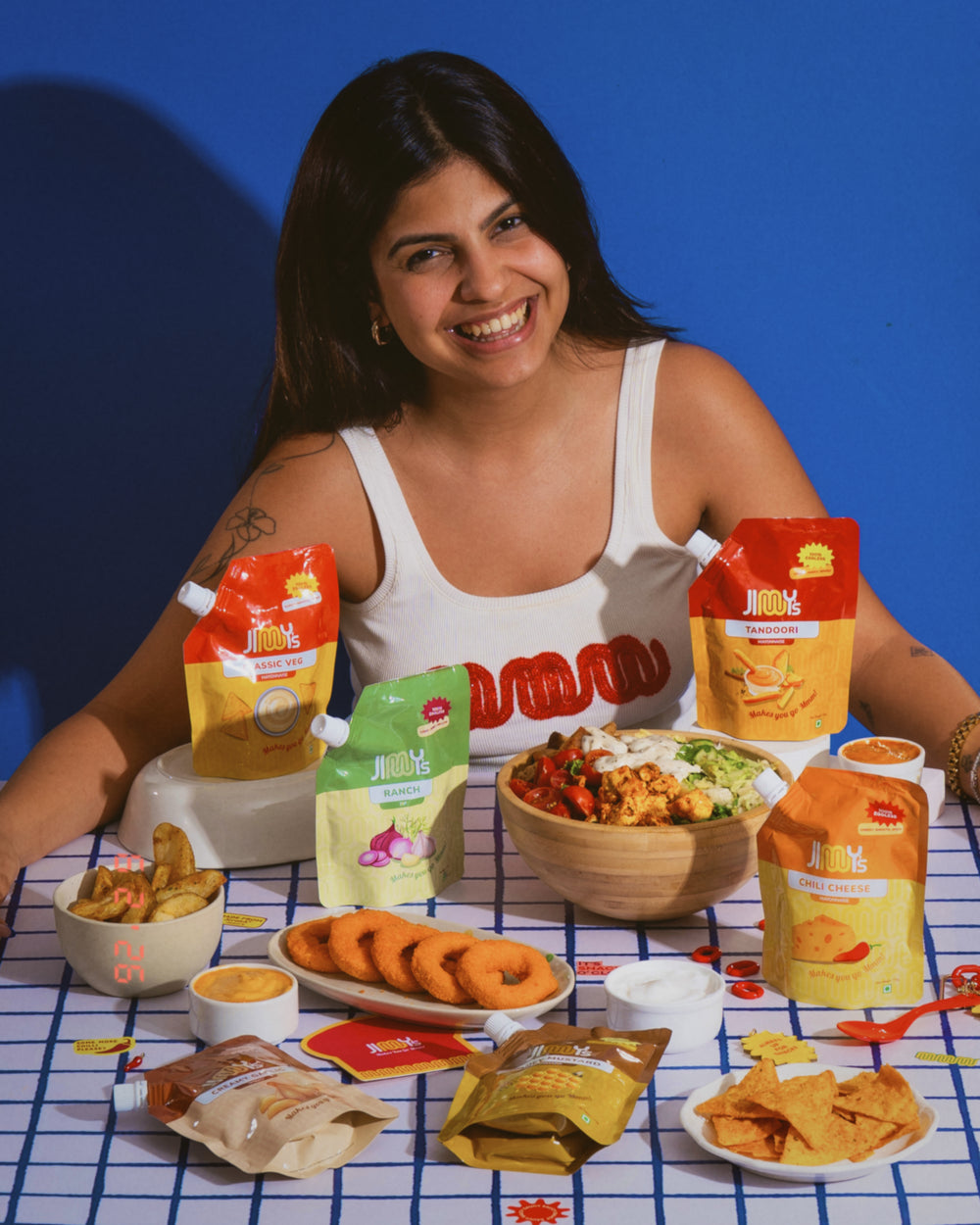 Woman with food items and packages on a checkered tablecloth against a blue background